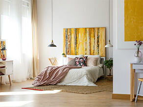 yellow feature artwork on white walls with hanging lights timber floor plants and pink pillows